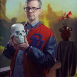 A white person with short hair wearing a letter jacket and holding a skull